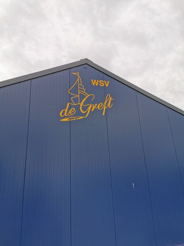 Refecterende gele logo bij Jachthaven de Greft